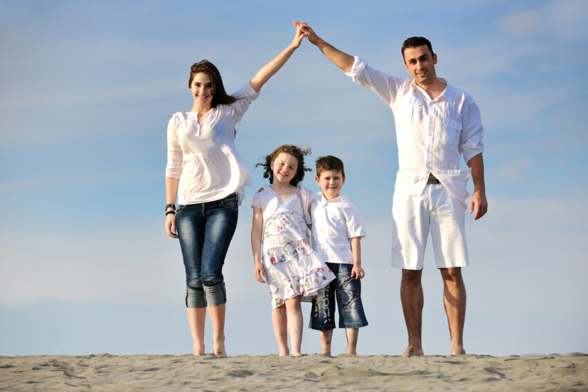 family on beach showing home sign