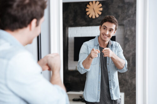 graphicstock smiling young man pointing fingers at his mirror reflection while standing at home B G0UO3I2g