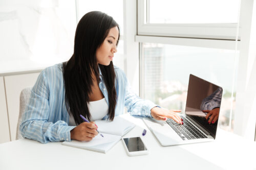 storyblocks young asian woman working with laptop and taking notes while sitting at the table indoors BCNHWyaa9Z