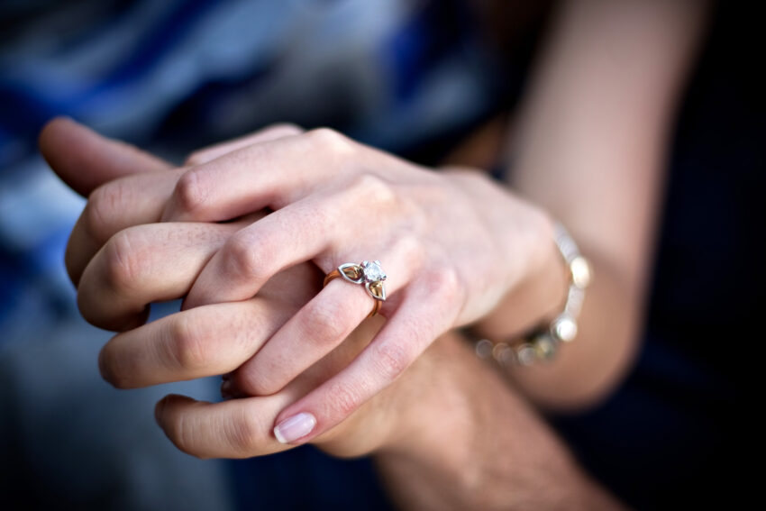 close up of a young couples hands and diamond engagement ring with platinum and gold accents shallow depth of field BtE8q0Hs